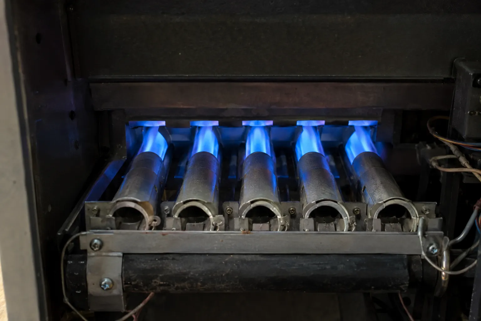 A row of gas furnace burners with blue flames